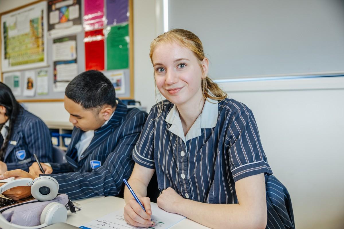 A student writing at her desk beside classmates in class, linking to enrolments at ACC Bairnsdale.