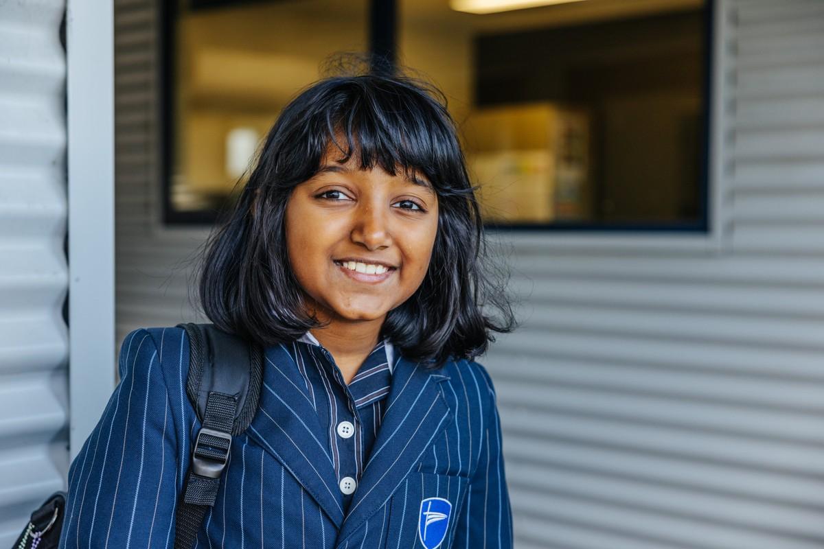 A smiling student in a striped school blazer carrying a backpack, linking to primary school at ACC Bairnsdale.