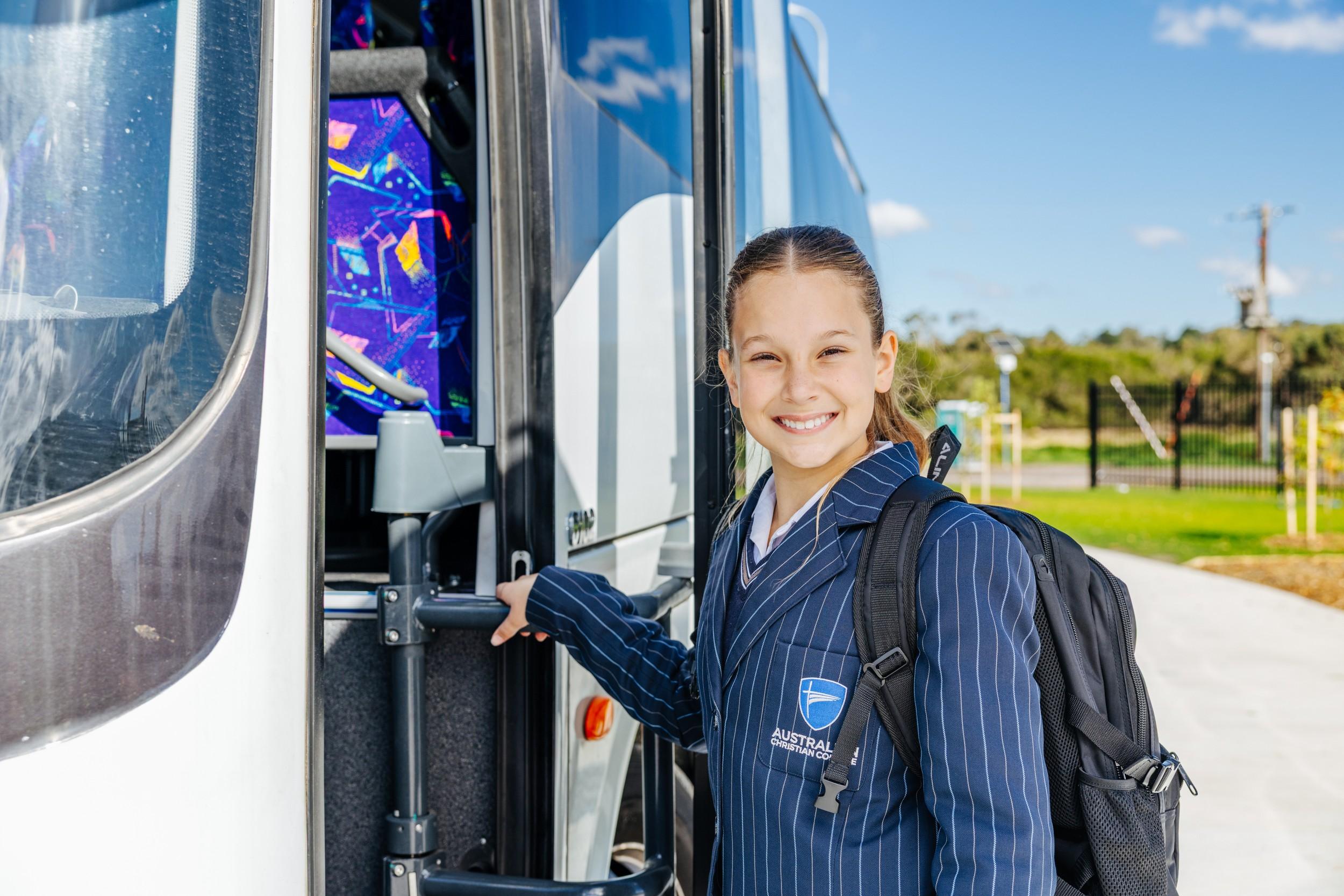 A smiling student with a backpack stepping onto an ACC Bairnsdale school bus.