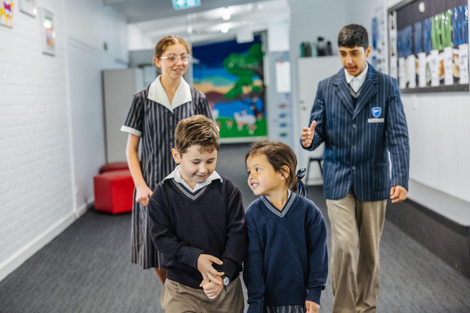 Two older students walking two younger students along a school corridor lined with student artwork.