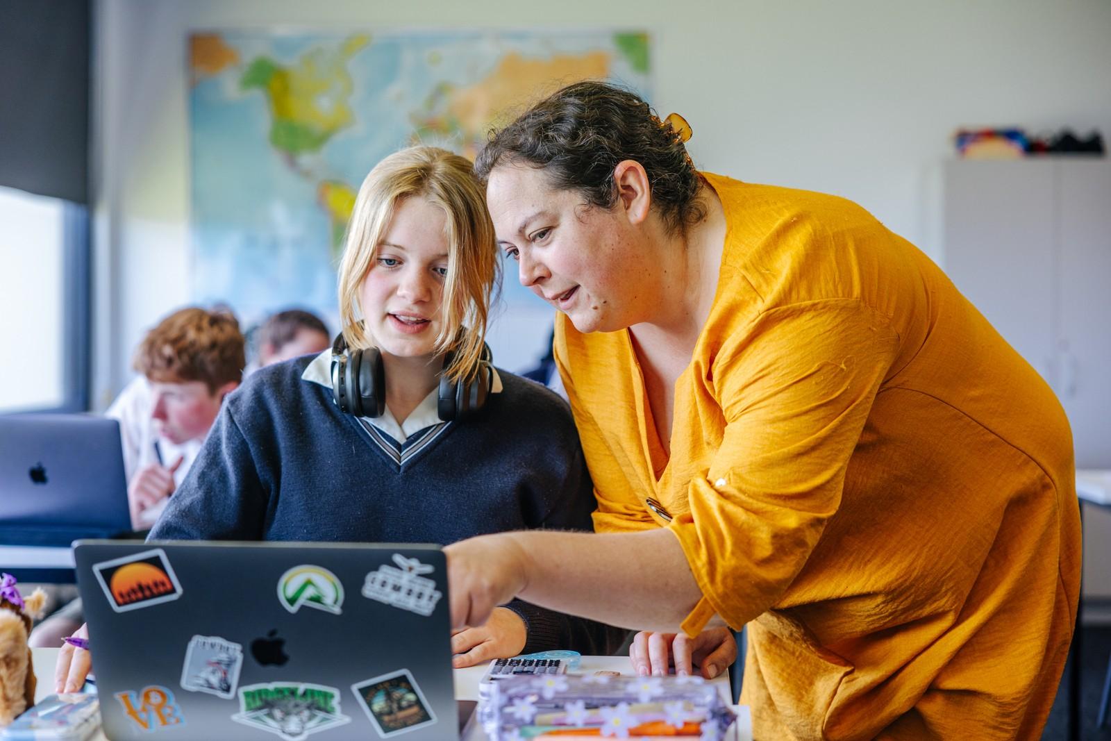 A teacher leaning in to help a secondary student with work on a laptop at ACC Bairnsdale.