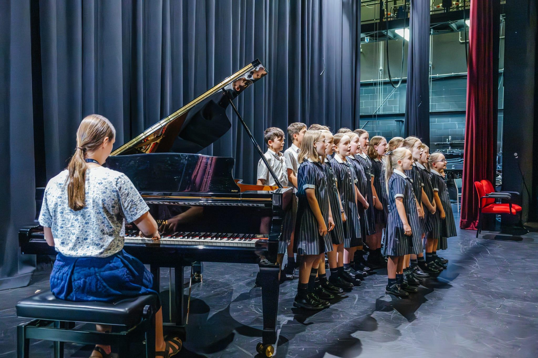 Primary school choir singing on stage with a student playing piano, showcasing performing arts at ACC Benalla.
