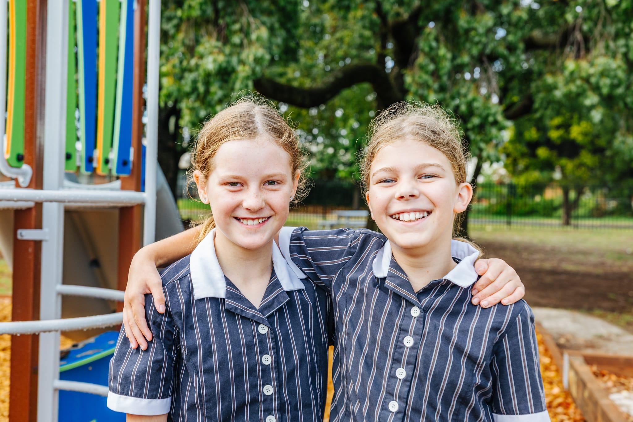 Two female primary students in uniform with arms around each other on a playground at Australian Christian College Benalla.