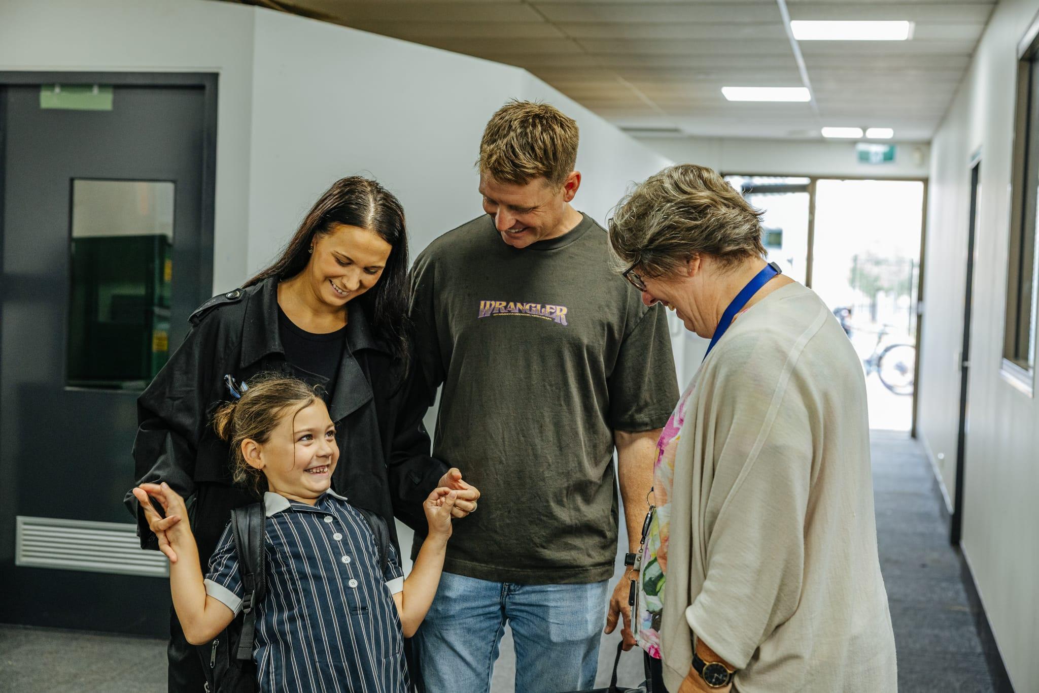 A family and a primary school student happily interacting with a teacher in the hallway at ACC Benalla, highlighting strong school-family partnerships.