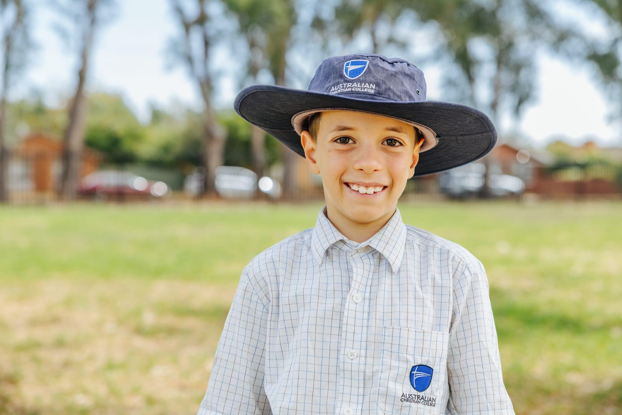 A smiling primary school student in uniform wearing a broad-brimmed hat at Australian Christian College Benalla in Victoria.
