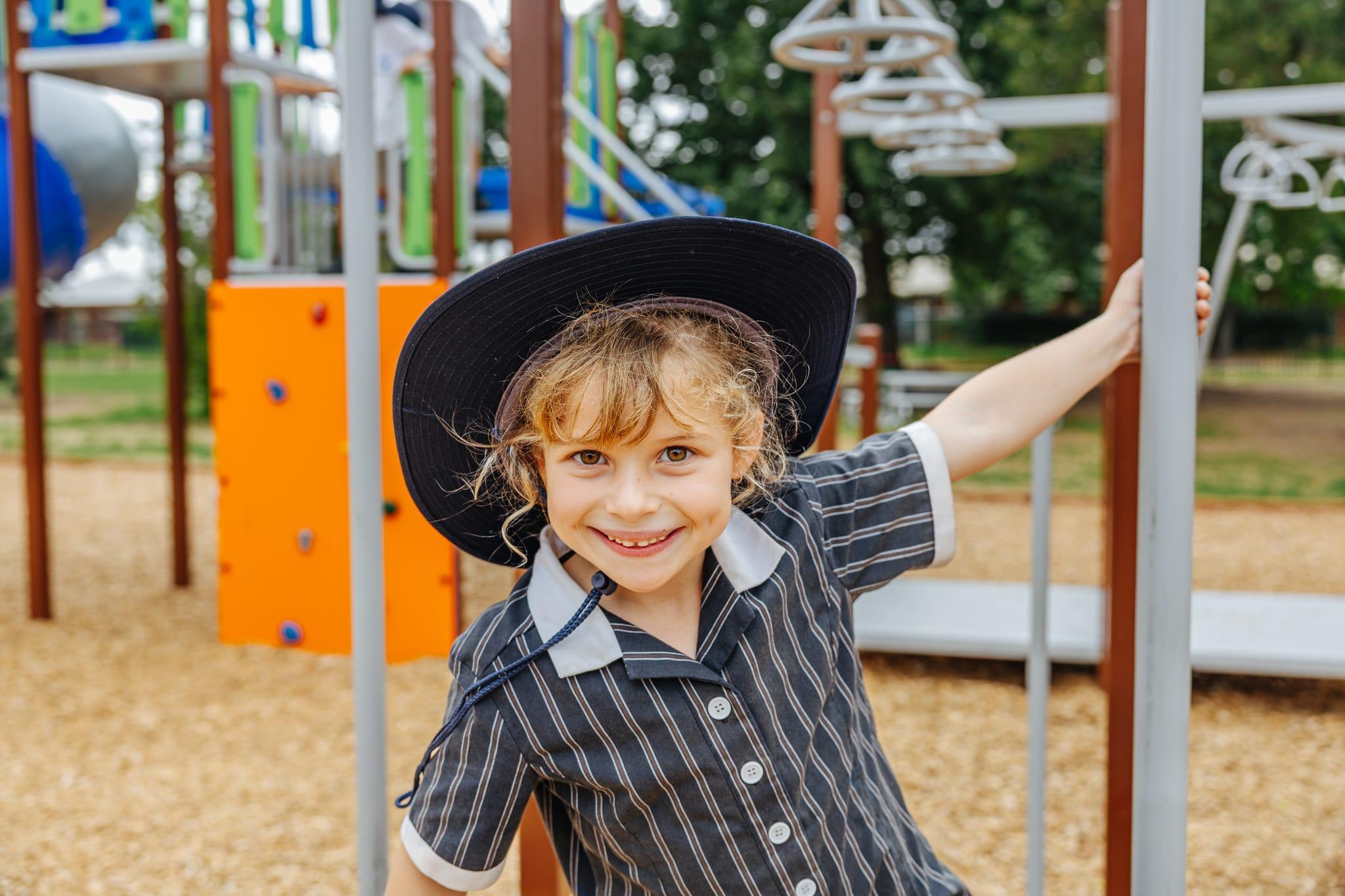 A happy primary school student in uniform and school hat on a playground at Australian Christian College Benalla, Victoria.