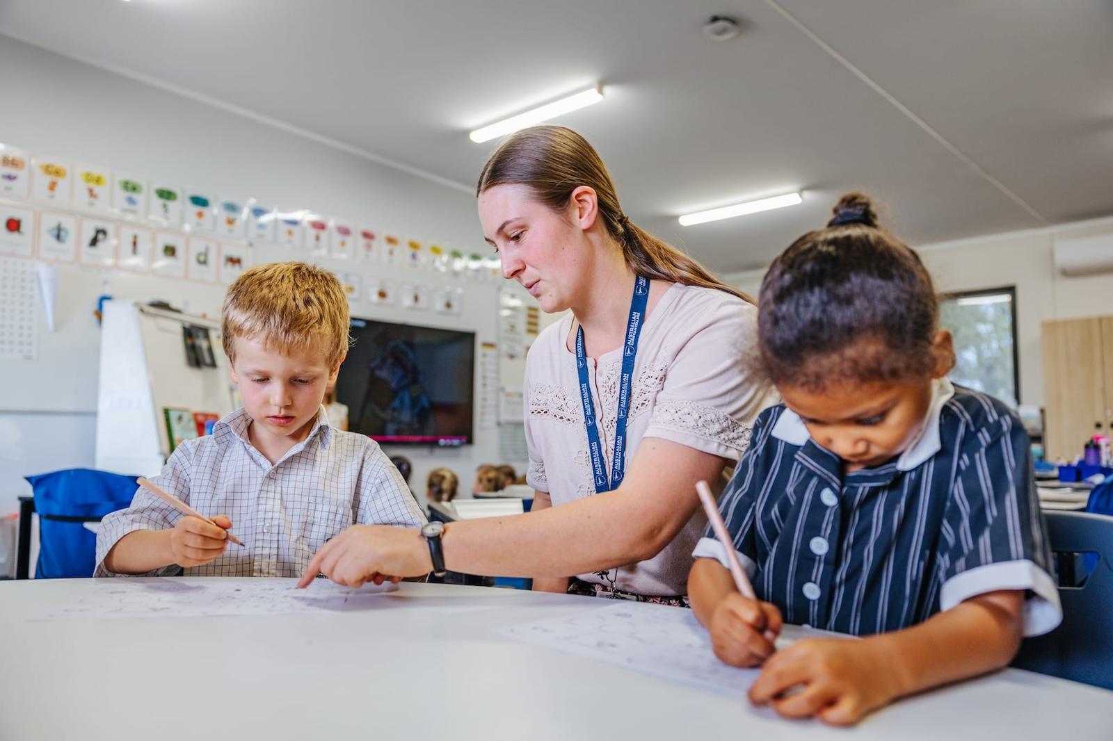 A dedicated teacher assisting two young primary school students with their work in a classroom at Australian Christian College Benalla, Victoria.