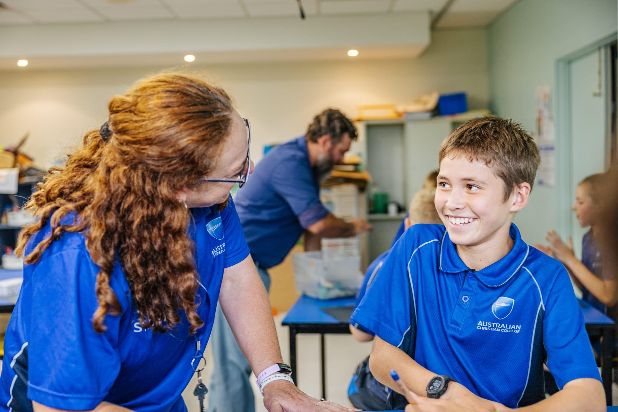 A teacher in a blue polo shirt engaging in a cheerful discussion with a male student in a classroom at Australian Christian College Benalla, Victoria.