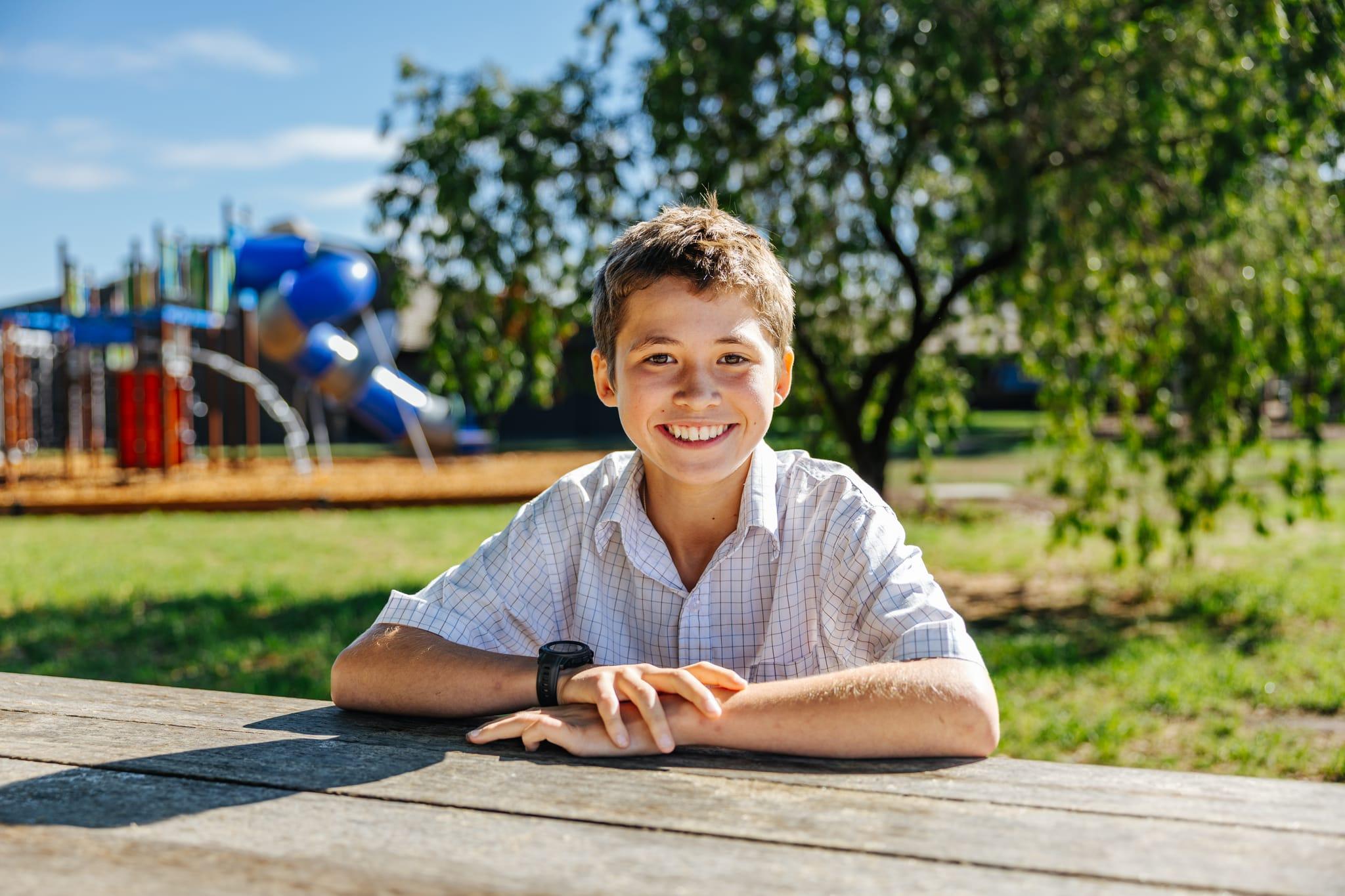 A smiling male student in a white collared shirt sitting a table outside at a Christian school in Benalla, Victoria.