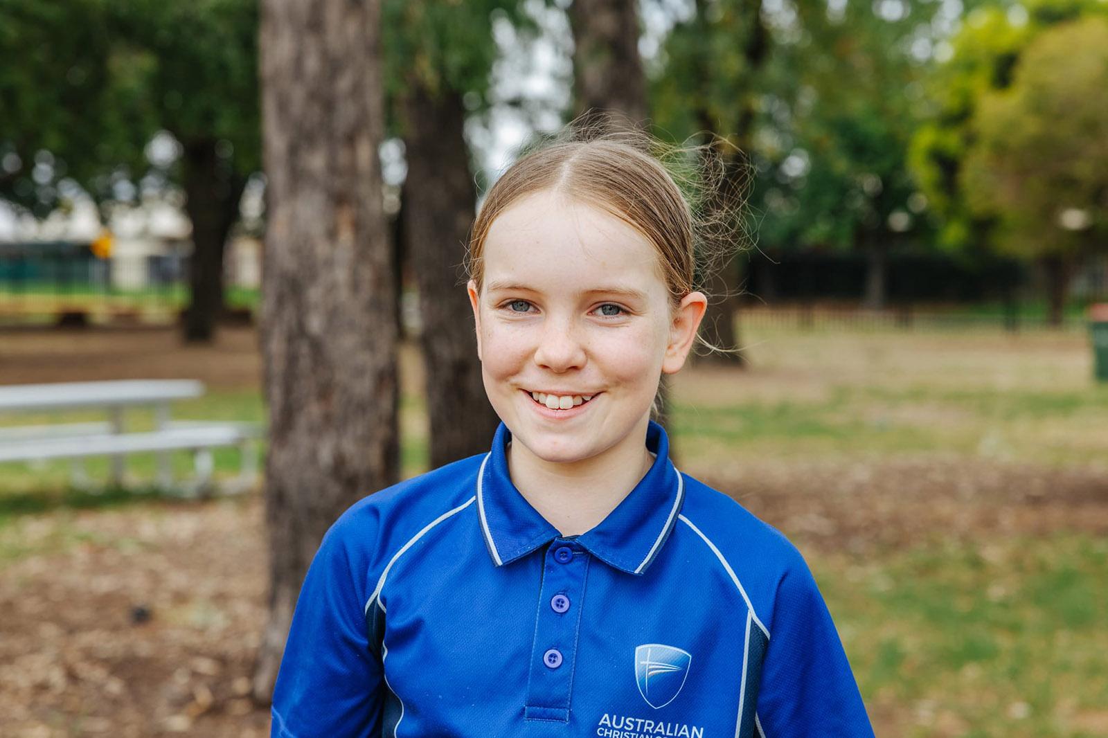 A smiling female Australian Christian College Benalla student in her blue uniform outdoors, serving as the hero image for forms and policies.