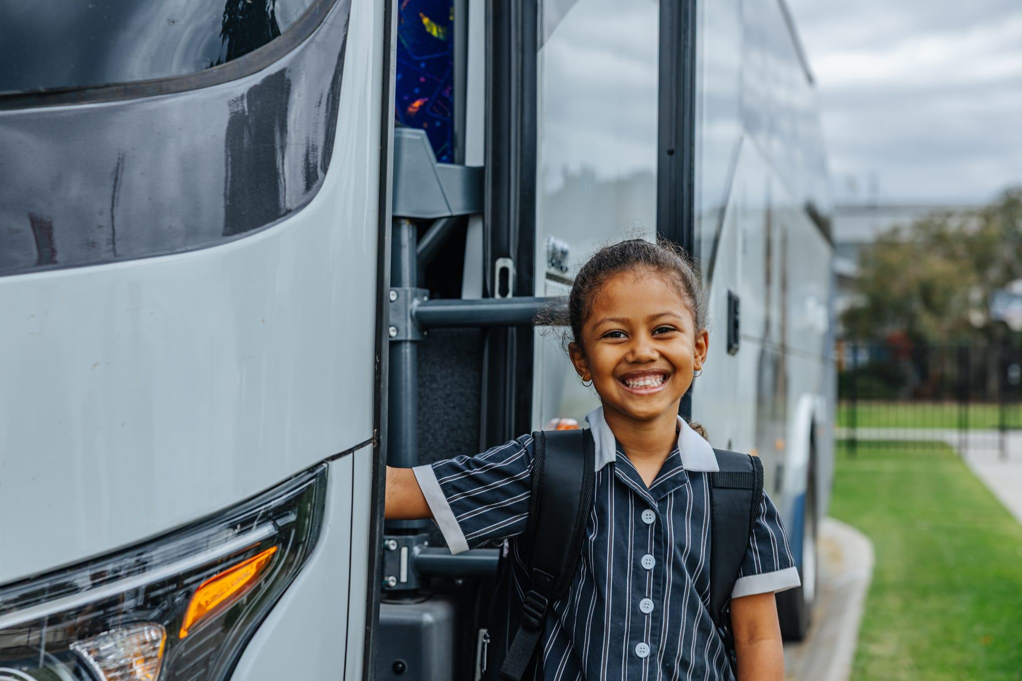 A happy Australian Christian College Benalla student smiling while standing next to a school bus, highlighting convenient bus routes.