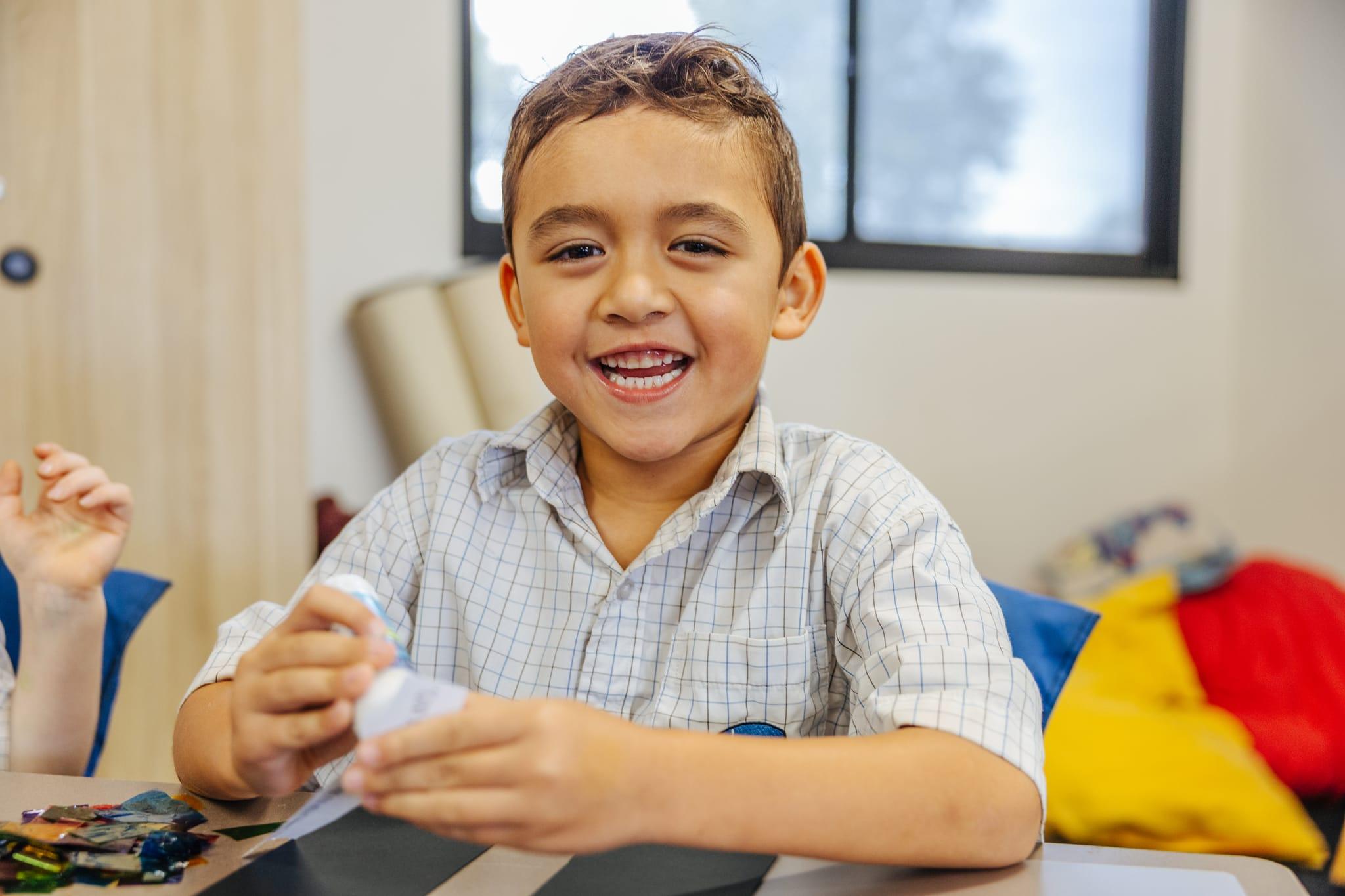 A joyful primary school boy at ACC Benalla smiling at the camera while participating in a hands-on classroom activity.