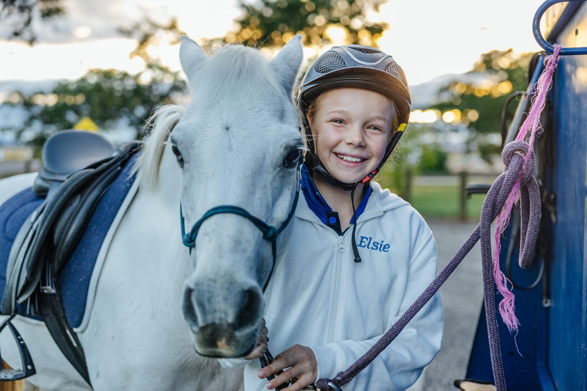 Smiling student wearing a helmet next to a white horse, showcasing equestrian co-curricular activities at ACC Benalla.