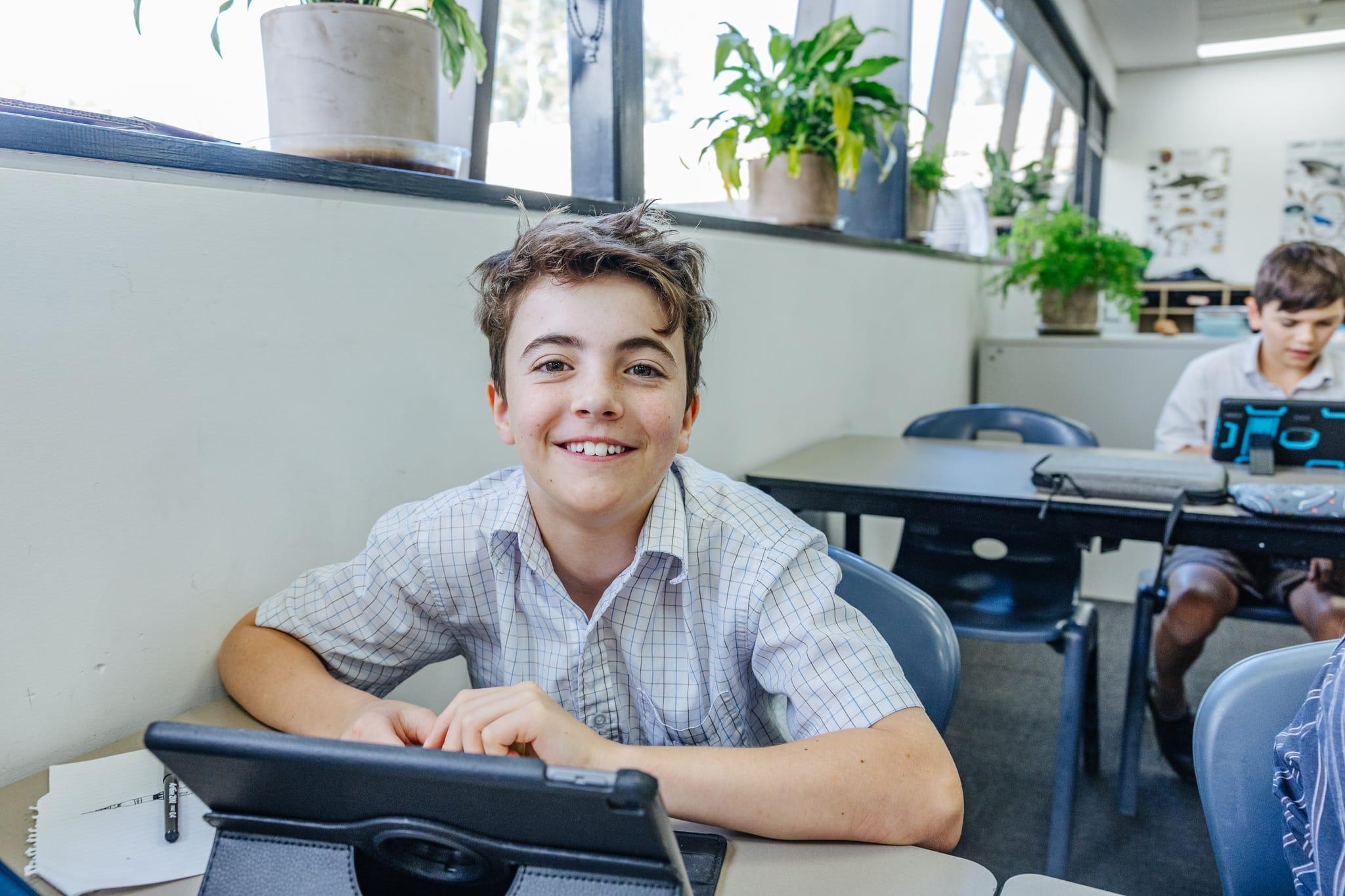 A happy male student at ACC Benalla looking at the camera while using a tablet in a bright classroom, representing accessible forms and policies.