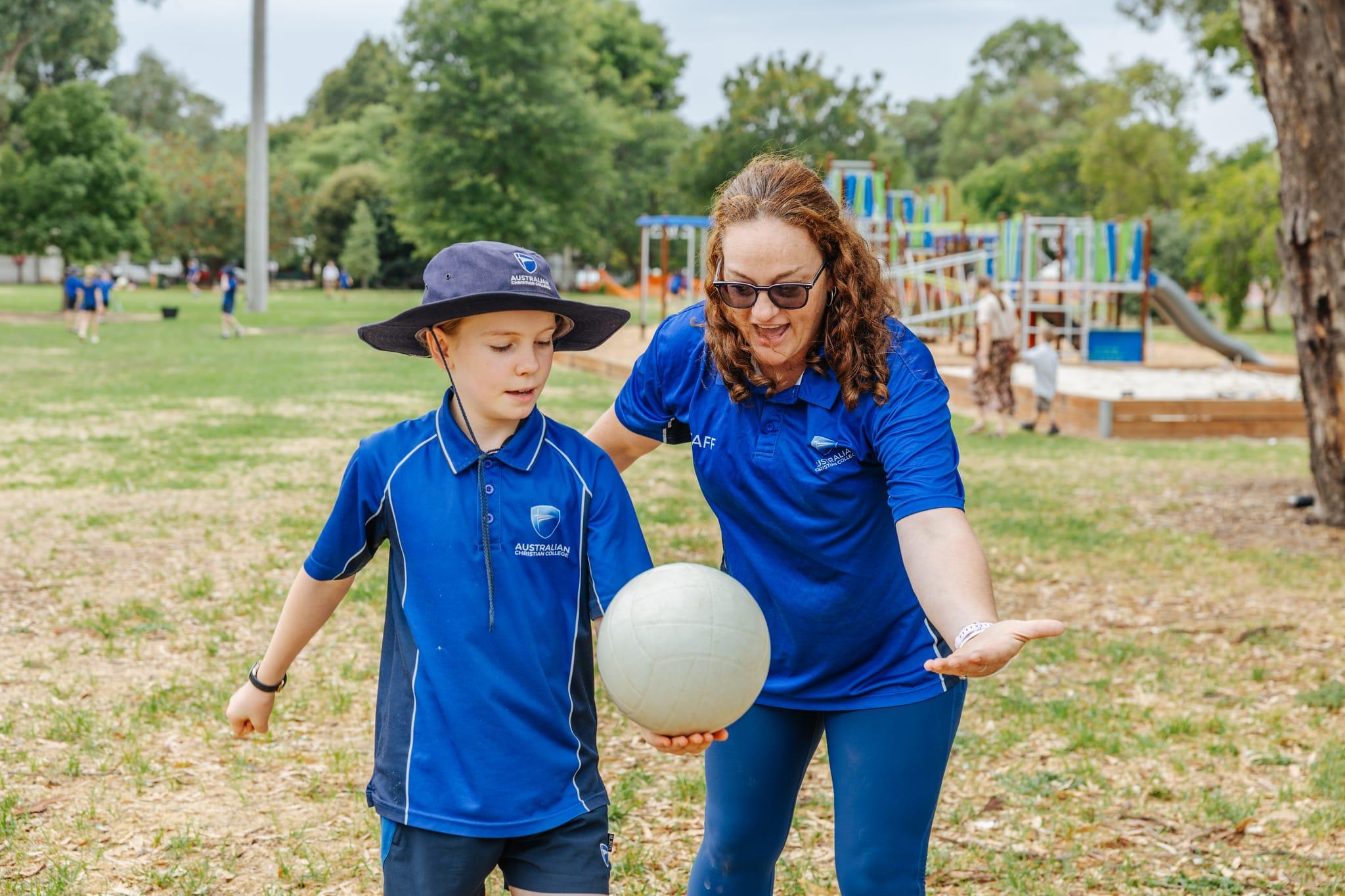 Teacher and primary school student with a ball on the sports field, demonstrating outdoor sports programs at Australian Christian College Benalla.