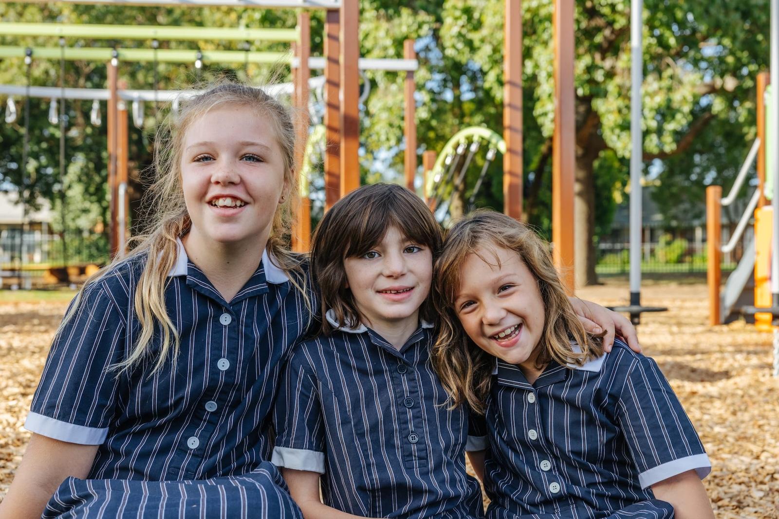 Three smiling Australian Christian College Benalla students on the school playground, inviting contact and community engagement.