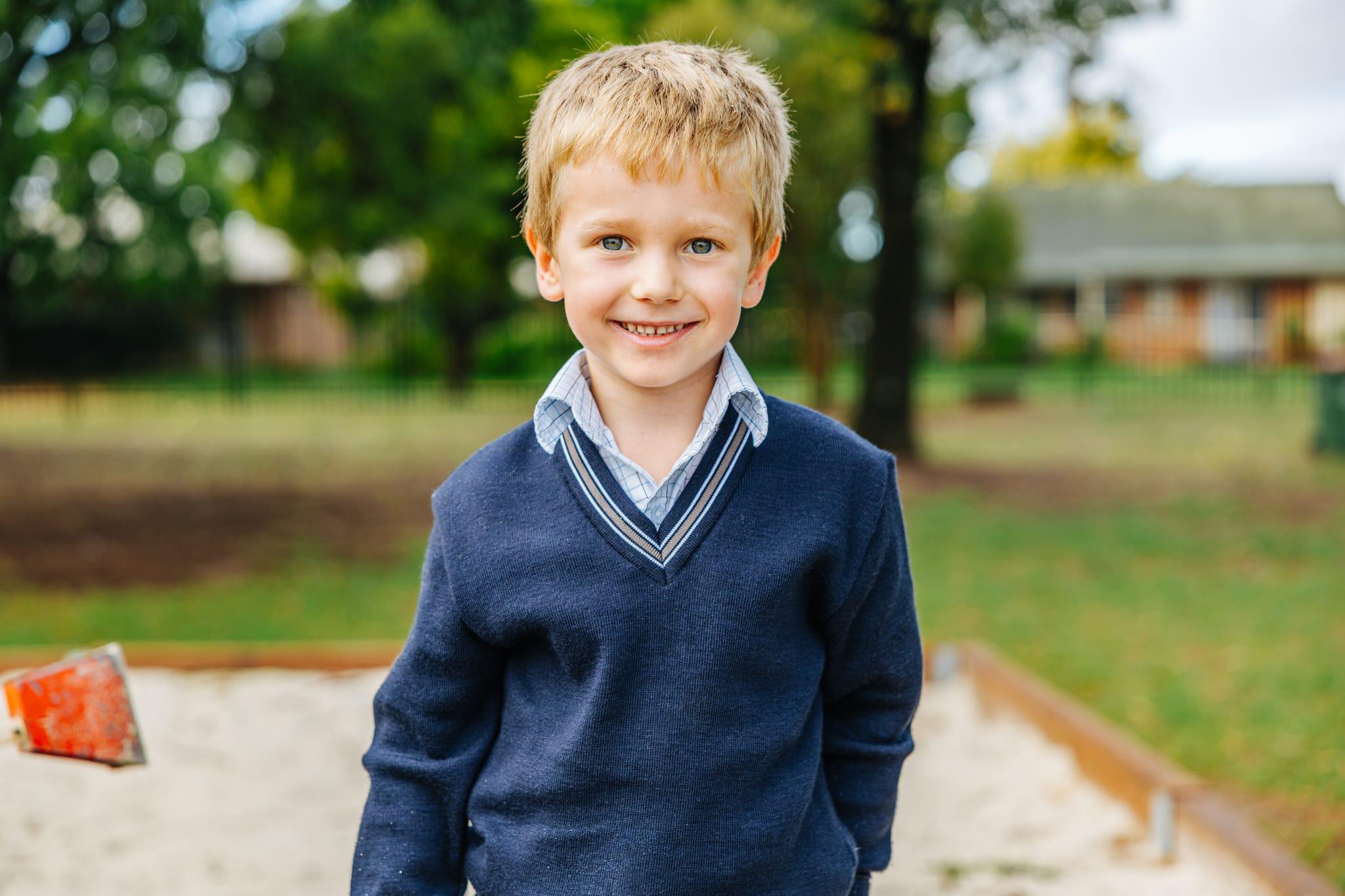 A well cared for, young male student in school uniform smiling at the camera on the school grounds of Australian Christian College Benalla, Victoria.