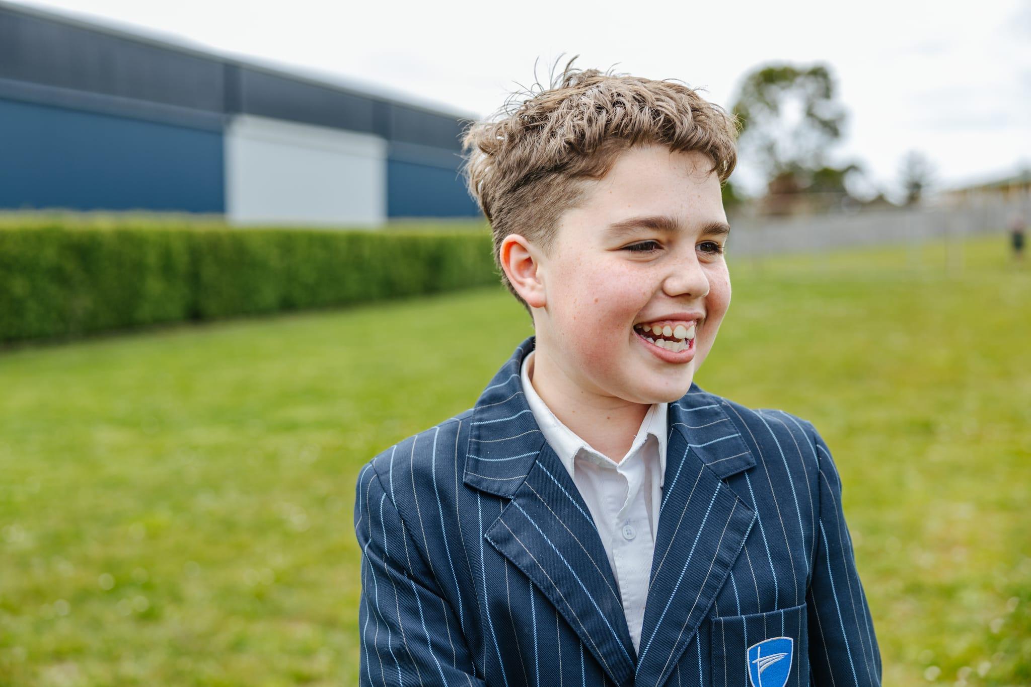 Smiling ACC Burnie student in navy pinstripe blazer laughing on the school oval in Somerset, Tasmania