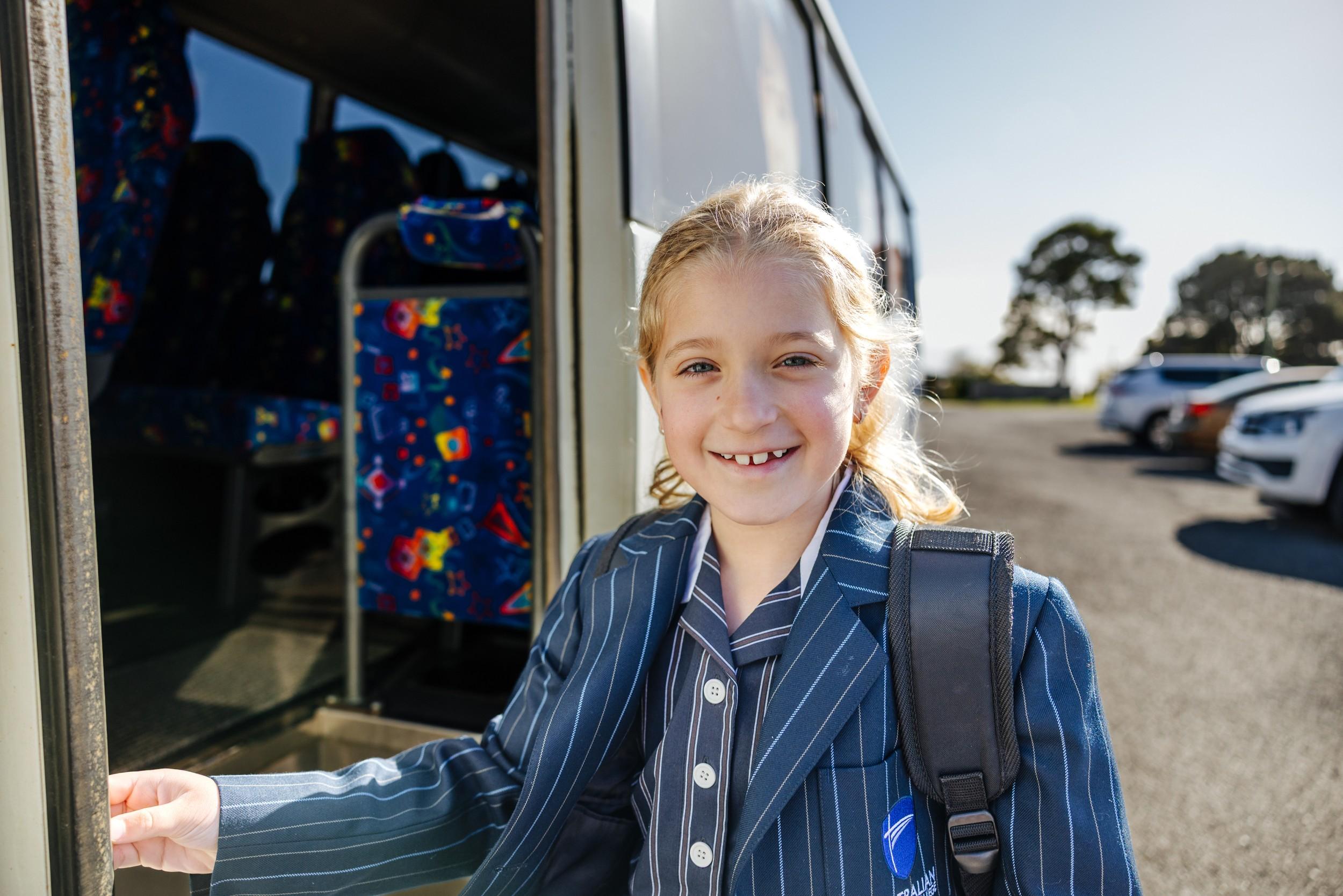 Smiling ACC Burnie student in school uniform boarding the school bus on a sunny morning in Somerset