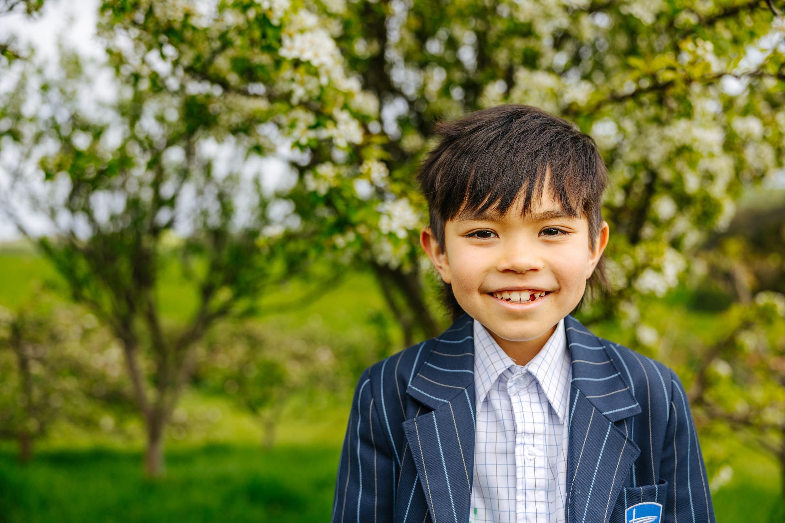 Smiling primary student in ACC Burnie uniform standing among blossoming orchard trees on the Somerset campus in Tasmania