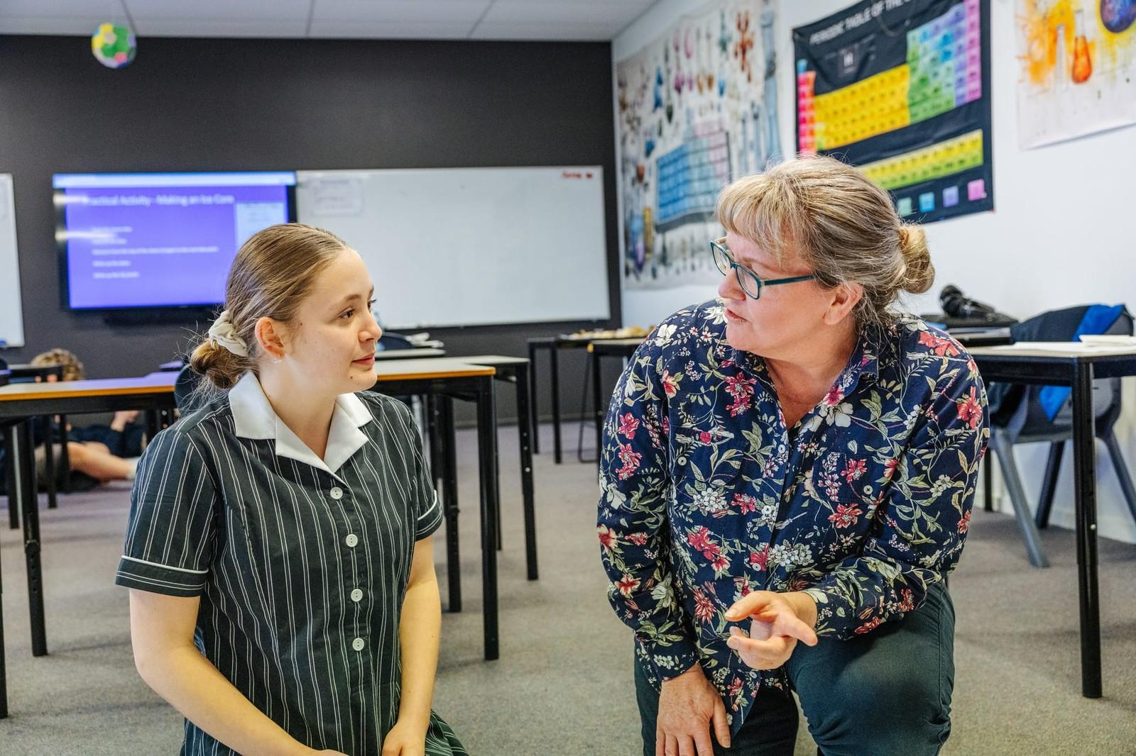 Two primary students smiling while writing on whiteboards at their desks in a bright Tasmania classroom, one wearing headphones.