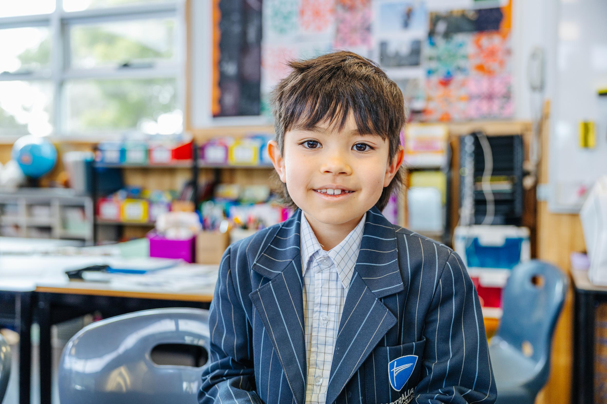 Primary boy holding headphones and a pencil, smiling confidently at his desk in an ACC Burnie classroom in Tasmania