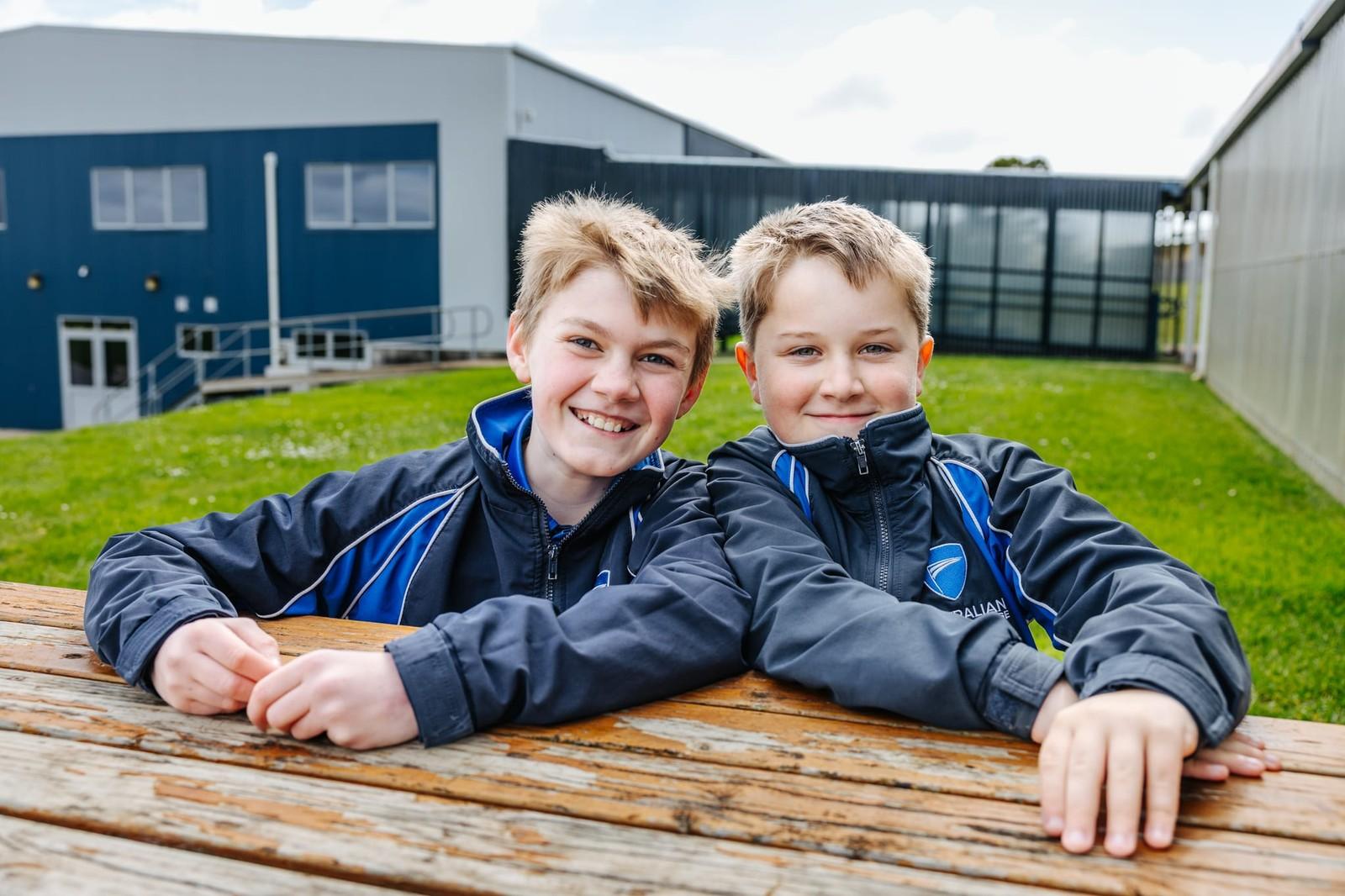 Two primary students leaning on an outdoor bench with ACC Burnie school buildings in the background
