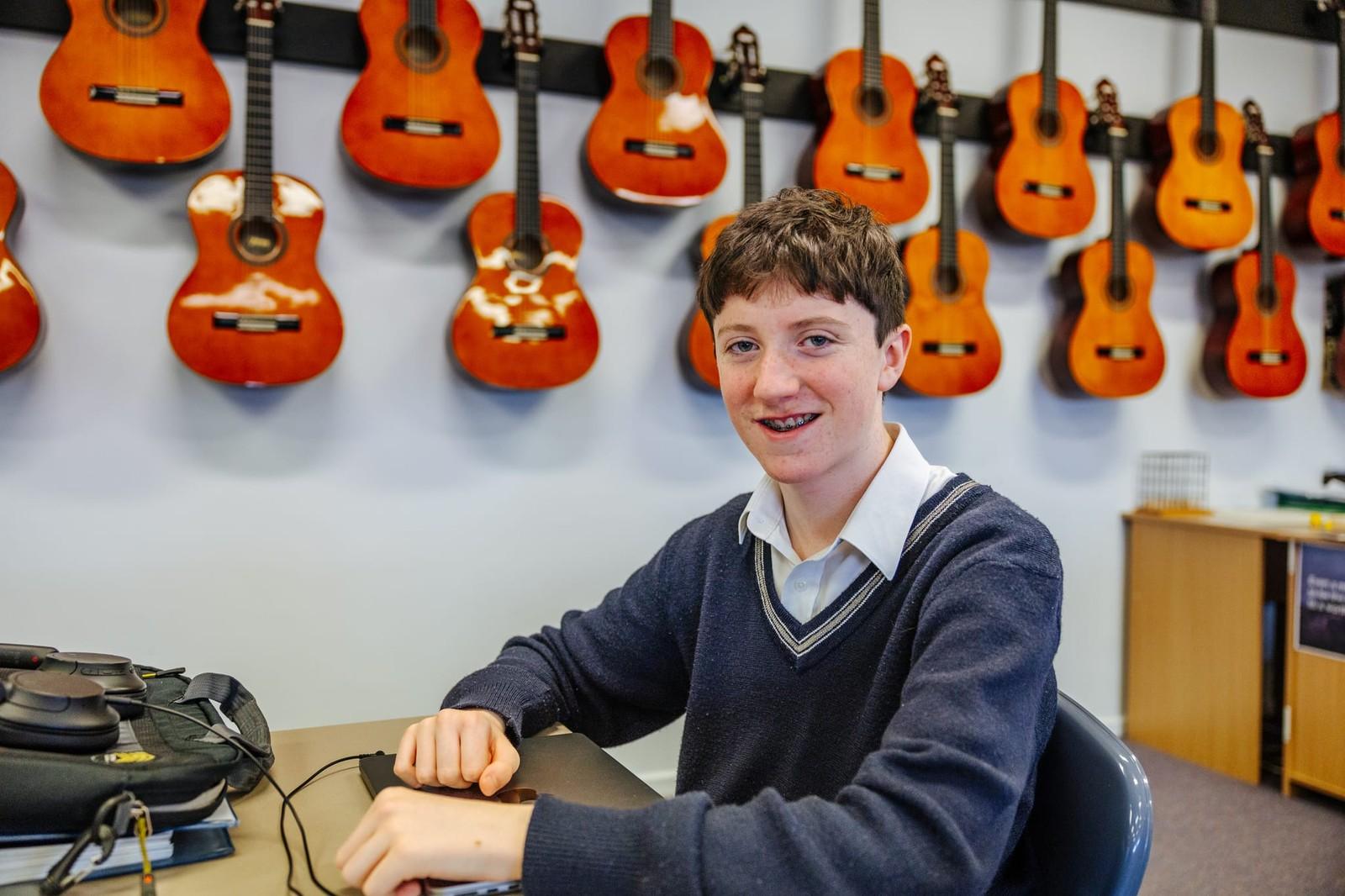 Secondary student seated in the music room with acoustic guitars on the wall at ACC Burnie in Somerset