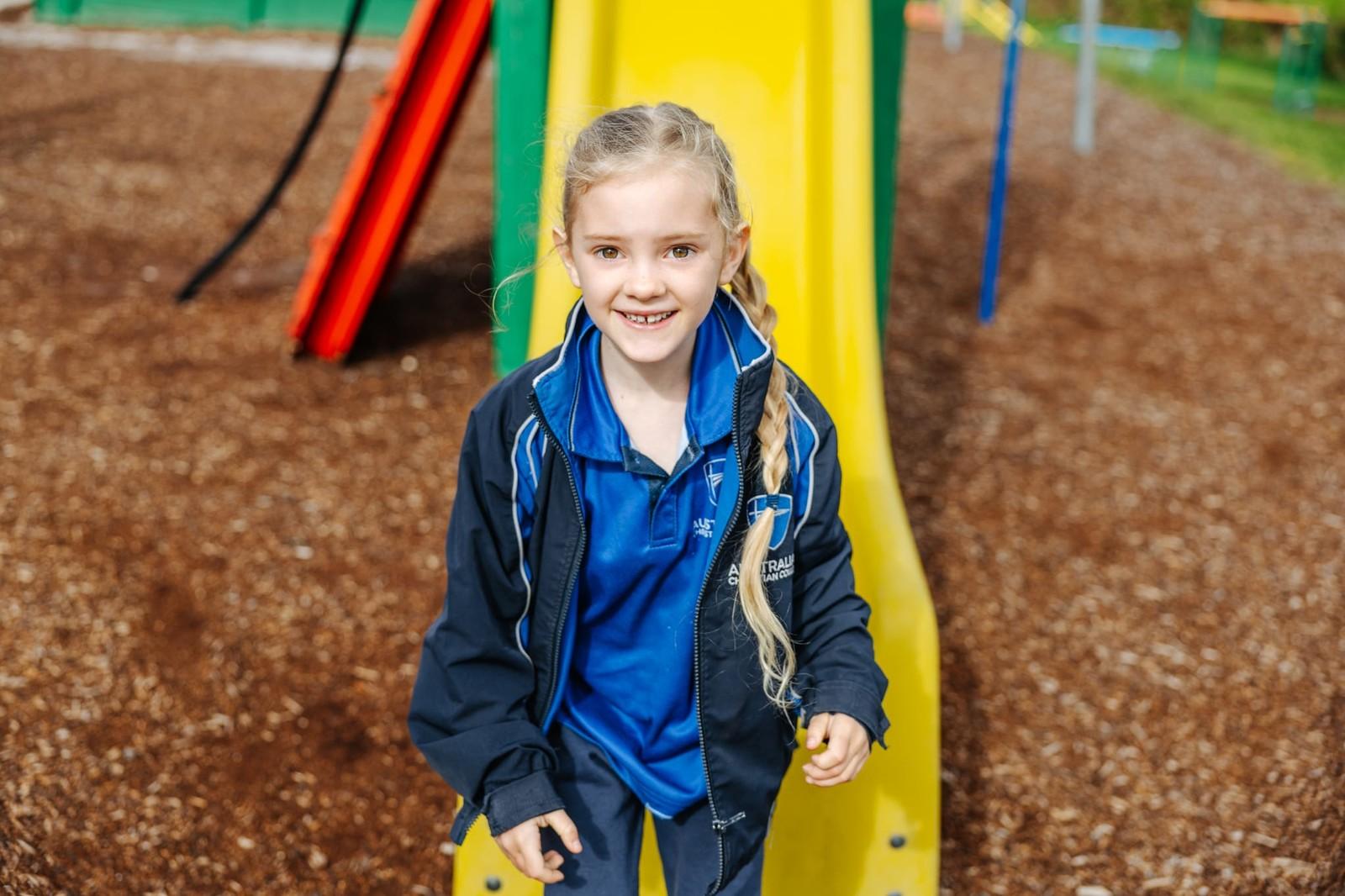 Smiling ACC Burnie primary girl at the base of a colourful playground slide during outdoor play