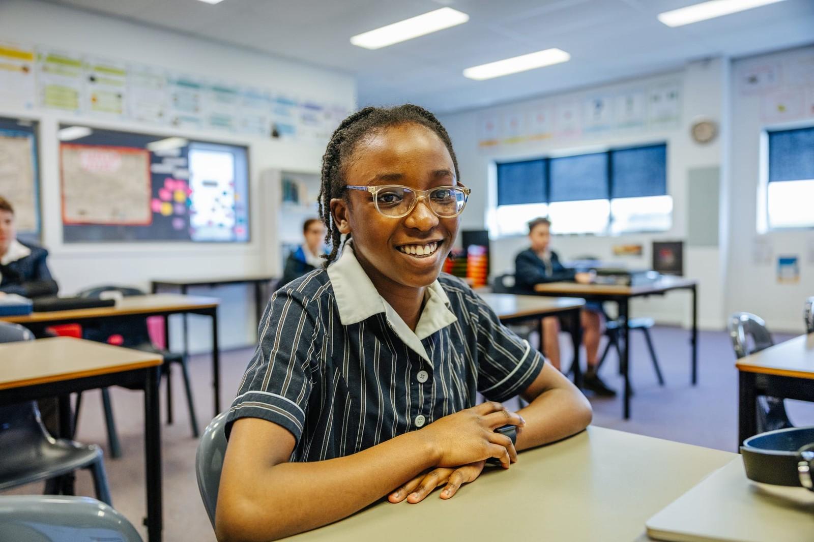 Secondary student with glasses smiling at her desk in a small class at ACC Burnie, Somerset