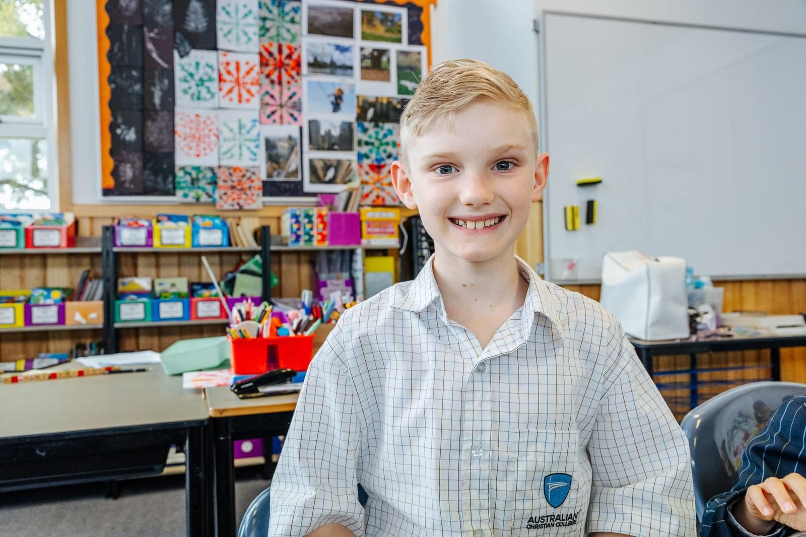ACC Burnie student smiling in front of a colourful student art display in his Somerset classroom