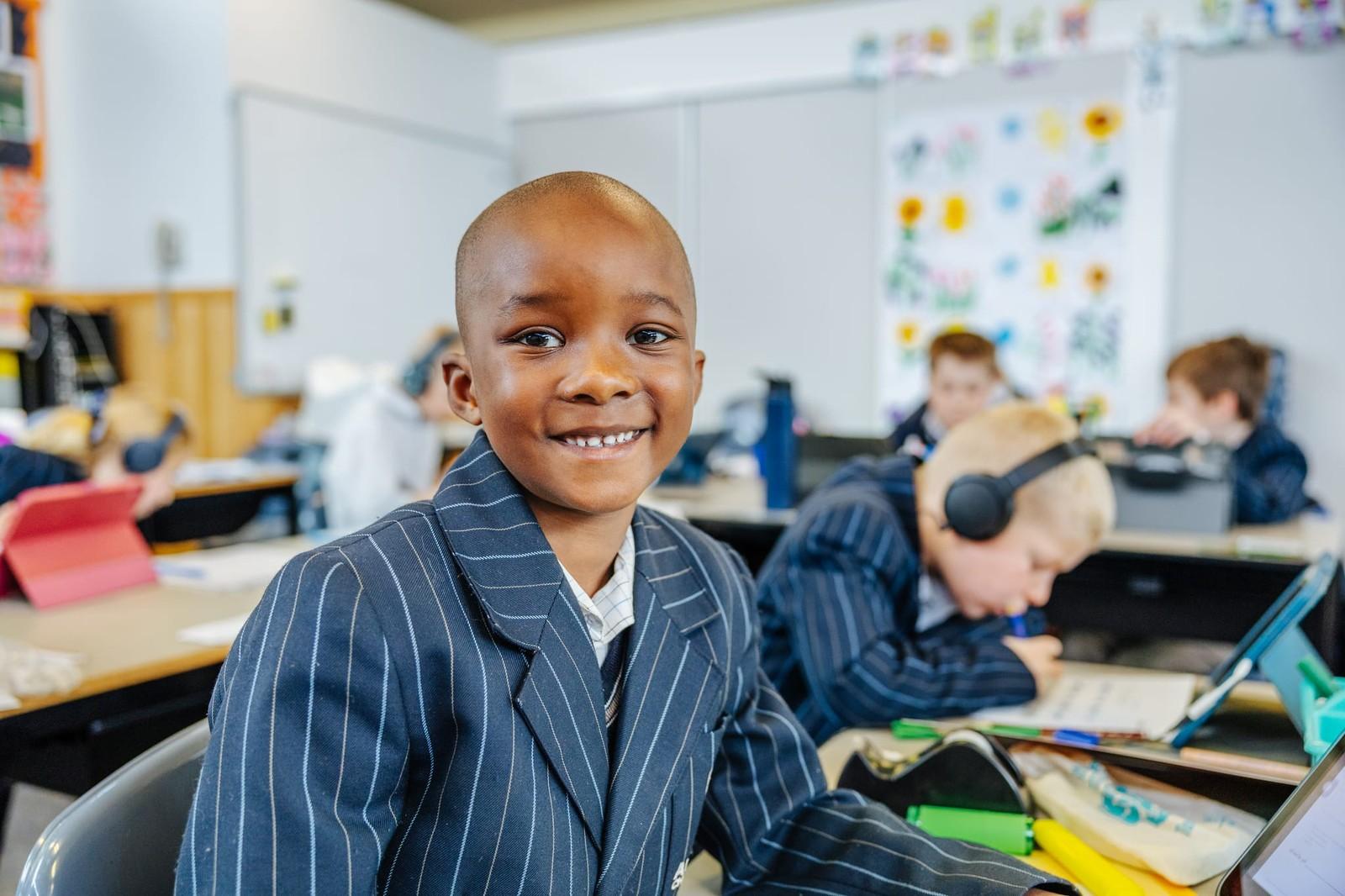Primary student smiling at his desk in a small, engaged classroom at ACC Burnie