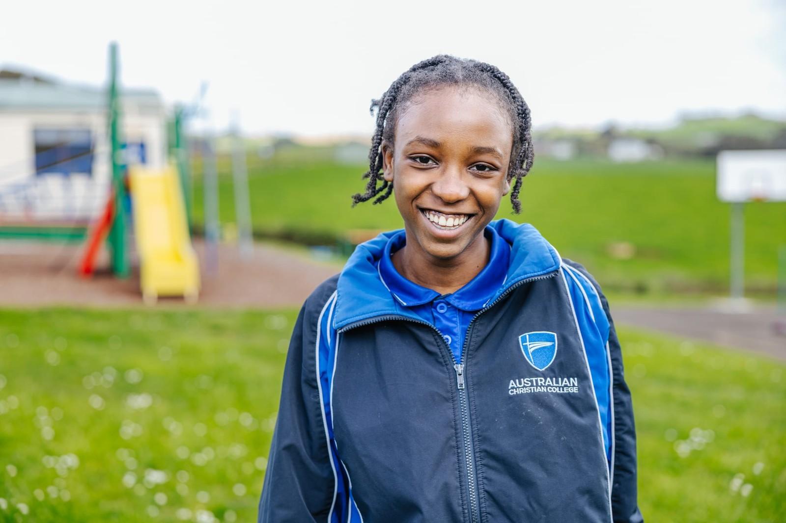 Smiling Australian Christian College student in blue sports jacket standing near the school playground in Somerset