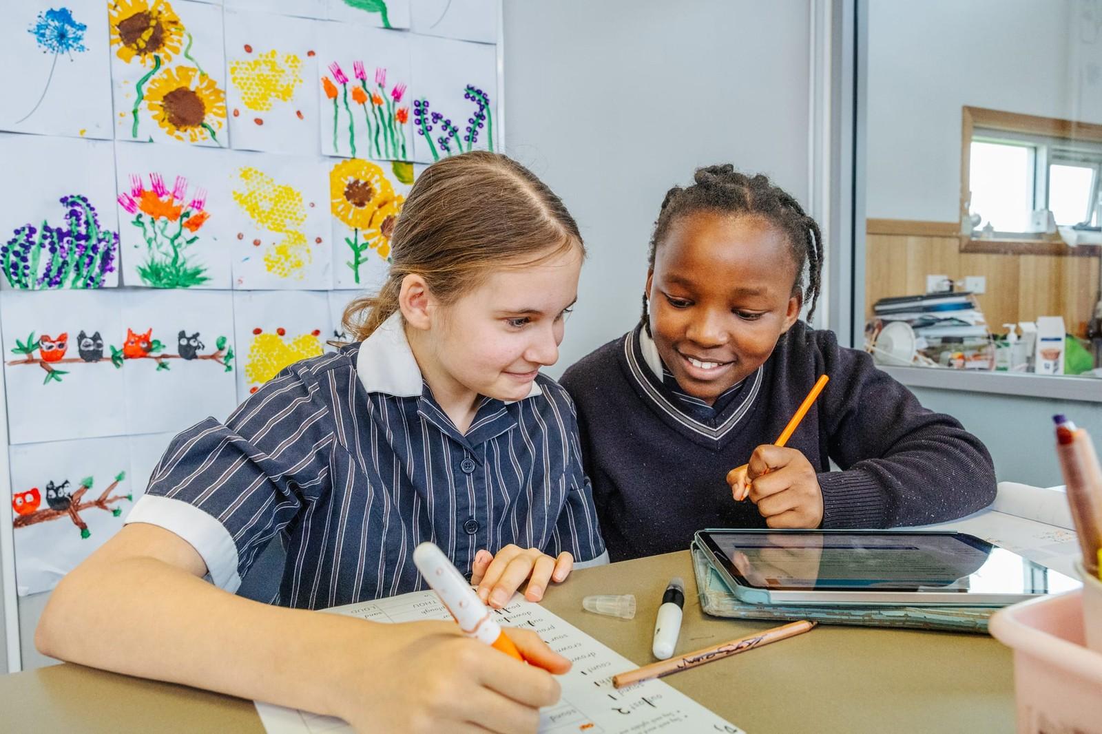 Two students collaborating with a tablet and markers in a colourful art-filled classroom at ACC Burnie.