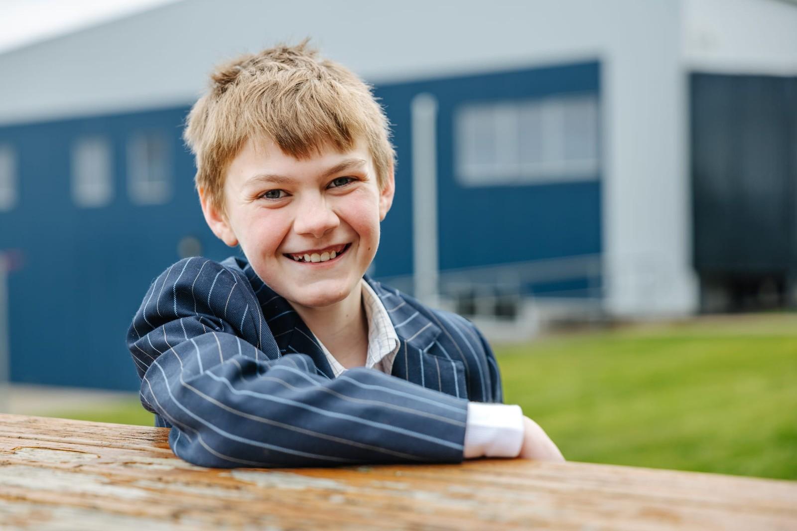 A smiling primary girl sitting on the grass in her school blazer at ACC Burnie in Somerset, Tasmania.