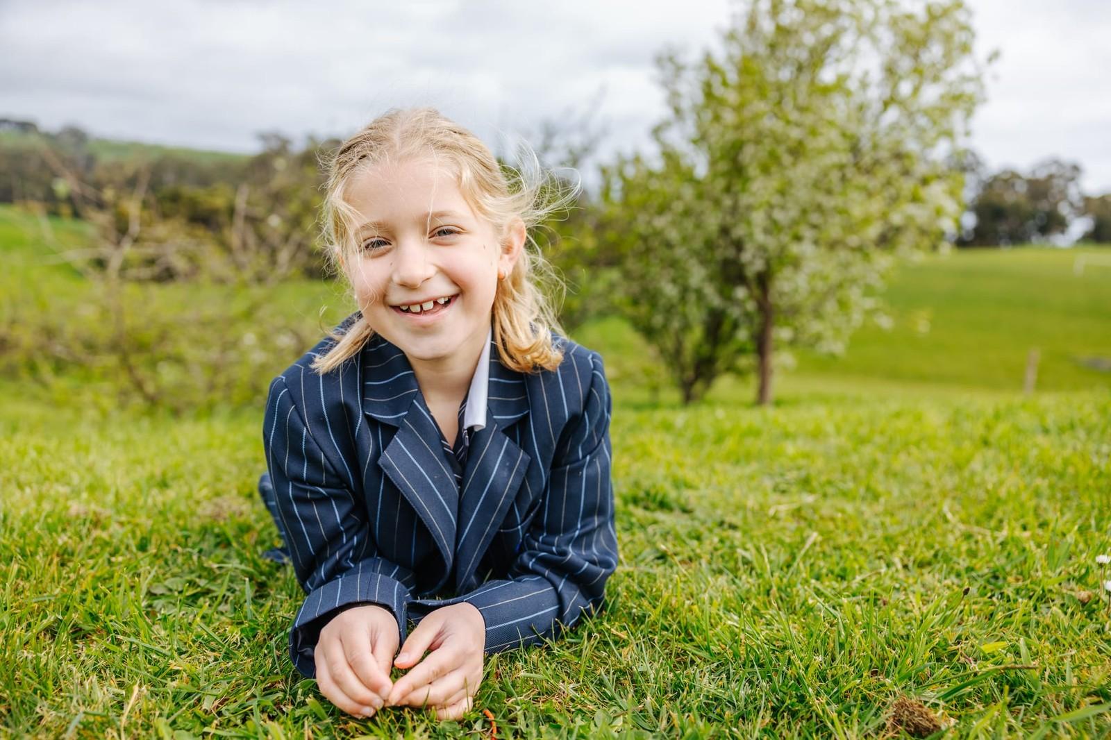 A smiling primary girl sitting on the grass in her school blazer at ACC Burnie in Somerset, Tasmania.