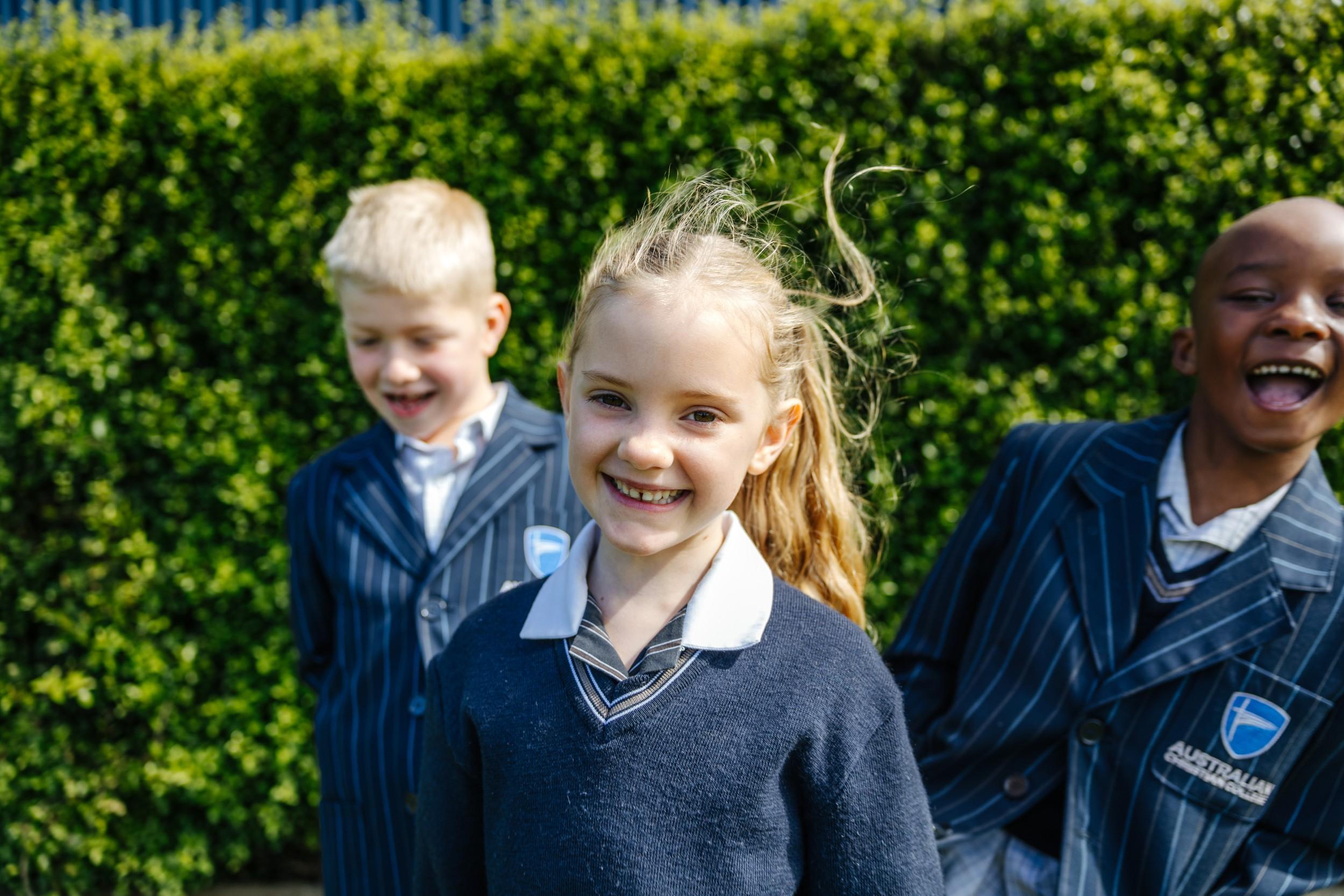 Three laughing primary students in uniform outdoors at ACC Burnie, a Christian school in Somerset, Tasmania.