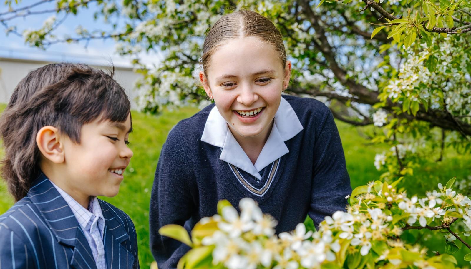 Two students laughing together among flowering trees on the grounds of Australian Christian College Burnie.