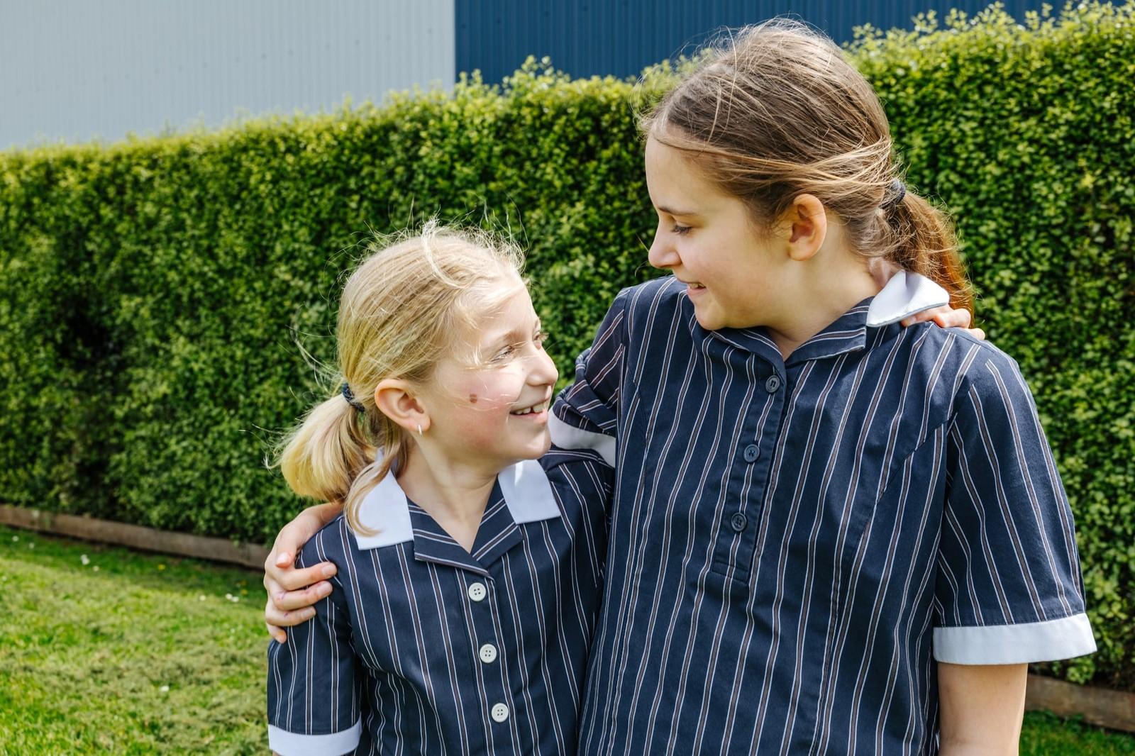 A girl and boy in ACC Burnie jackets crouching beside a garden bed, exploring plants together against a wide open Somerset landscape.