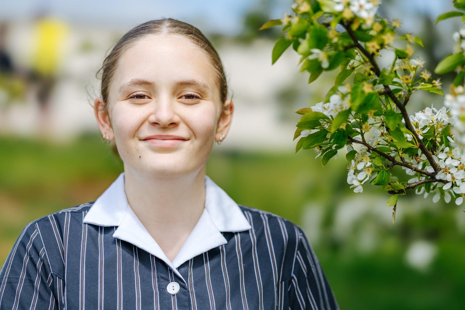 A secondary student in striped school uniform smiling beside a blossoming white-flower tree at ACC Burnie in Tasmania.