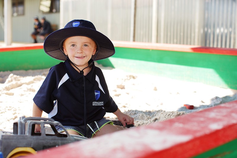 smiling boy wearing hat playing in sandpit
