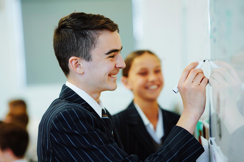 High school student smiling writing on whiteboard