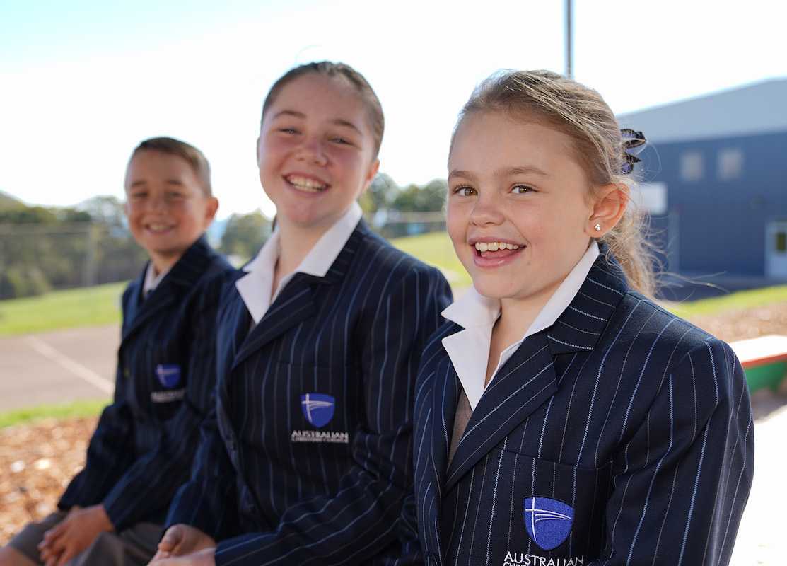 three happy ACC Somerset students sitting on a bench wearing school blazers