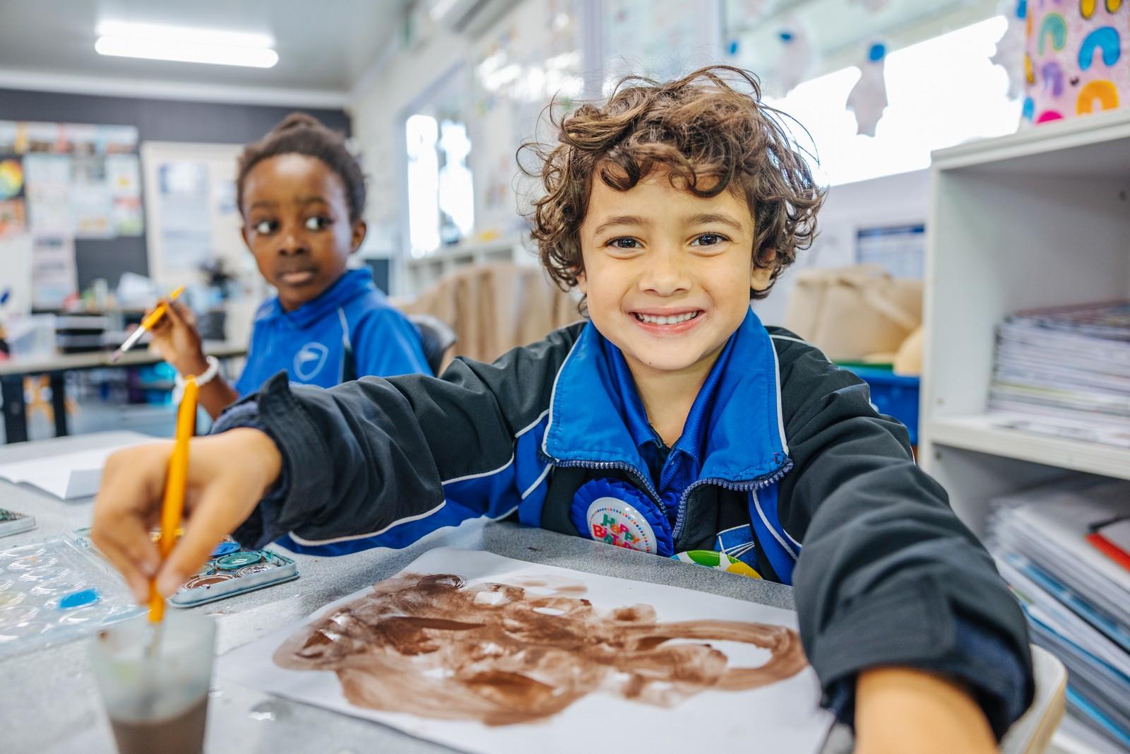 Kindergarten child paints at a table, refining fine motor skills through creative expression at ACC Darling Downs.