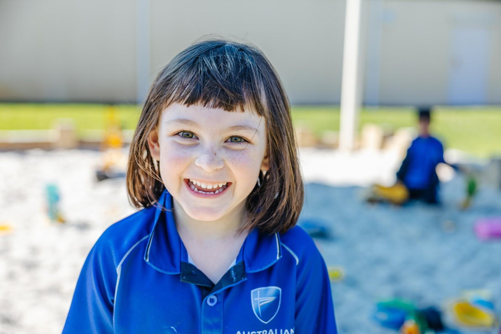 Kindergarten student smiles outside in the shade, enjoying a supportive early learning environment at ACC Darling Downs.