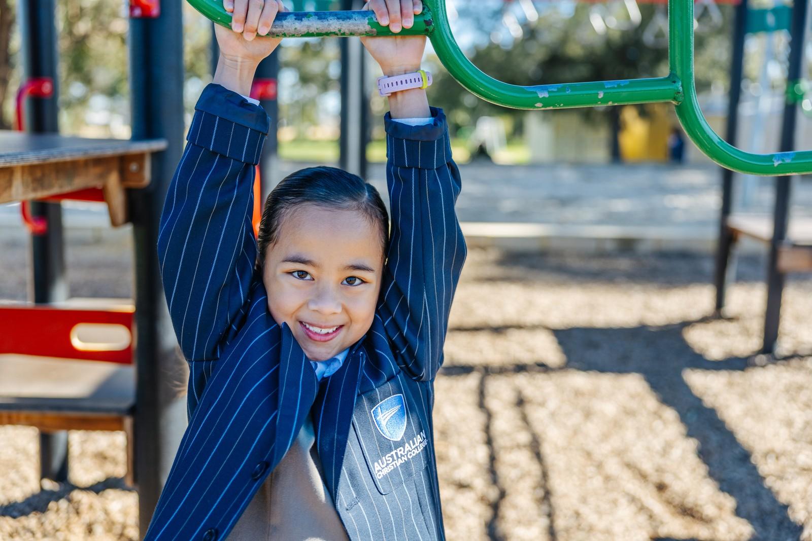 A primary student plays on the climbing equipment in the Darling Downs playground, reflecting an active, joyful start to school.