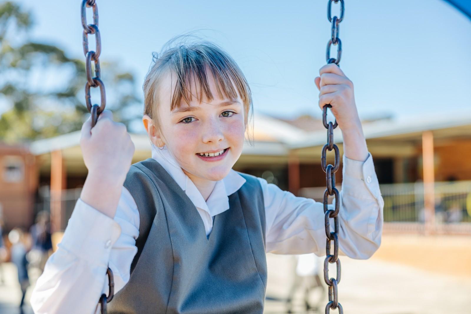 Primary student smiling on a playground swing during break time at Darling Downs.