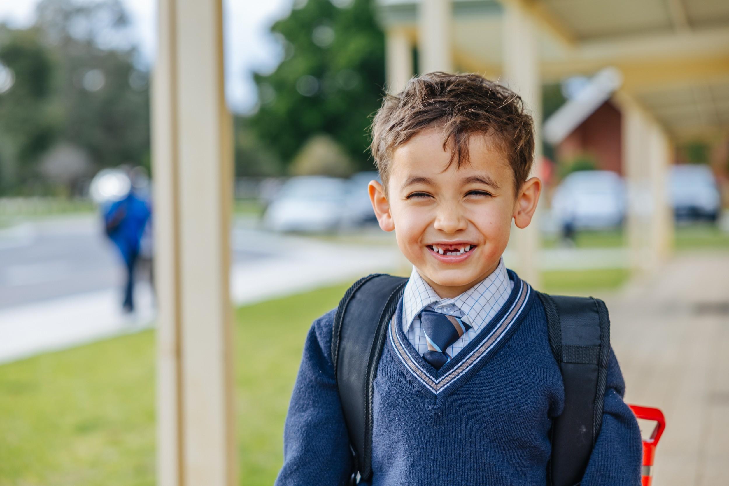 Smiling primary student in full uniform with backpack on campus at ACC Darling Downs, ready to start the school day.