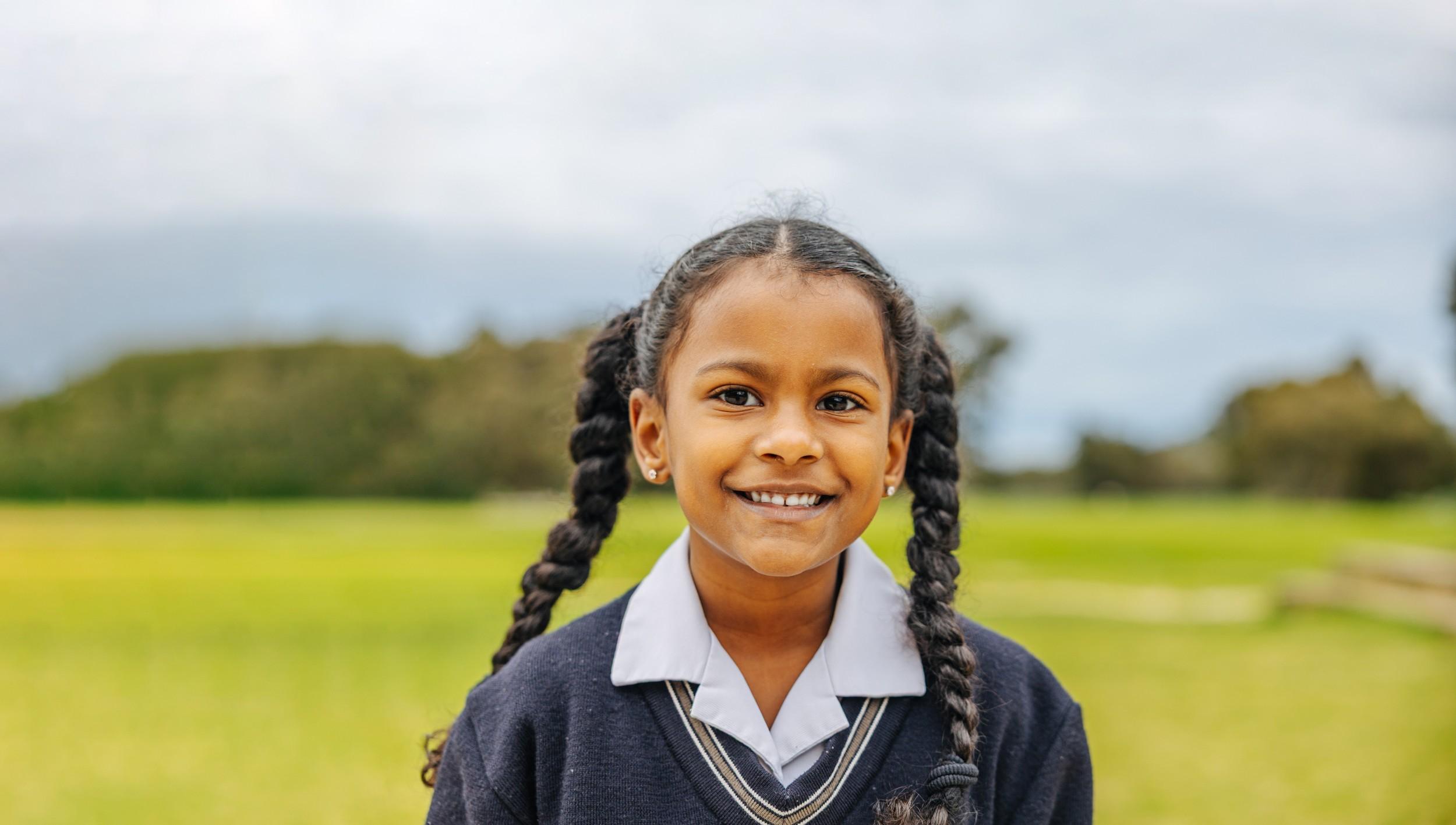Smiling primary student in ACC Darling Downs uniform standing on a grassy school field.