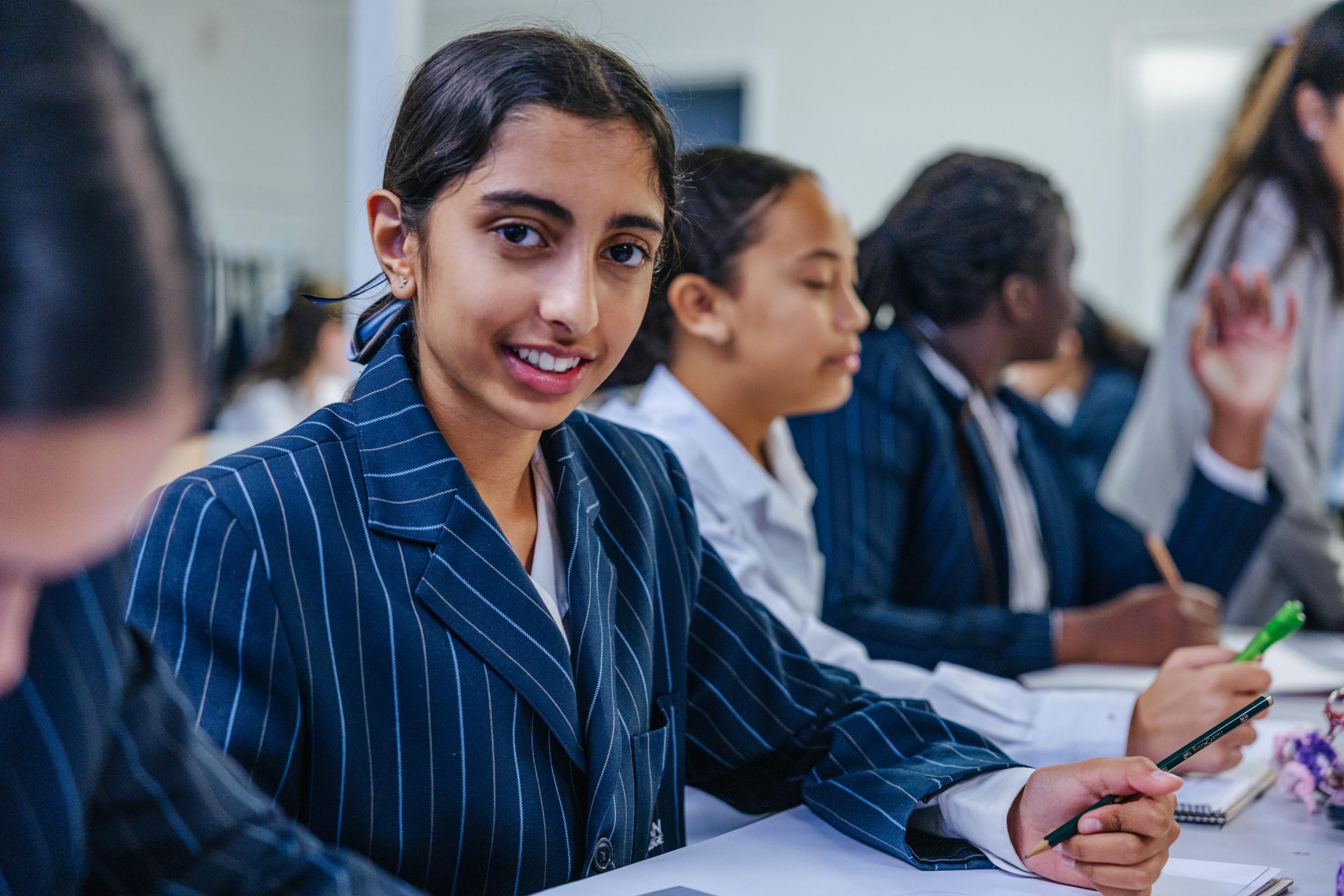 Secondary student smiling in a Darling Downs classroom as classmates take notes at their desks.